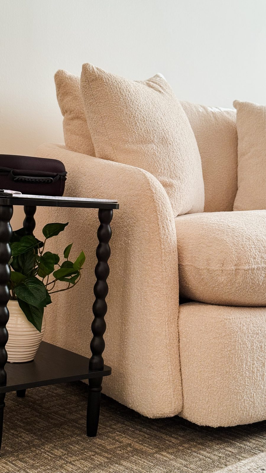 A cream boucle armchair beside a black spindle side table holding a potted plant