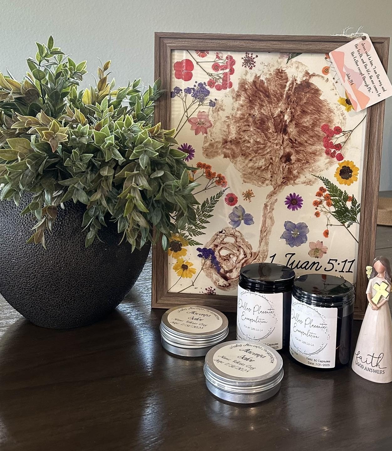 A framed placenta print decorated with pressed flowers beside jars of placenta capsules and tins of salve