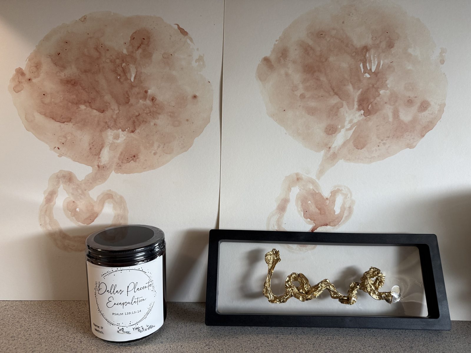 Two placenta prints behind a jar of Dallas Placenta Encapsulation capsules and a framed gold keepsake spelling love