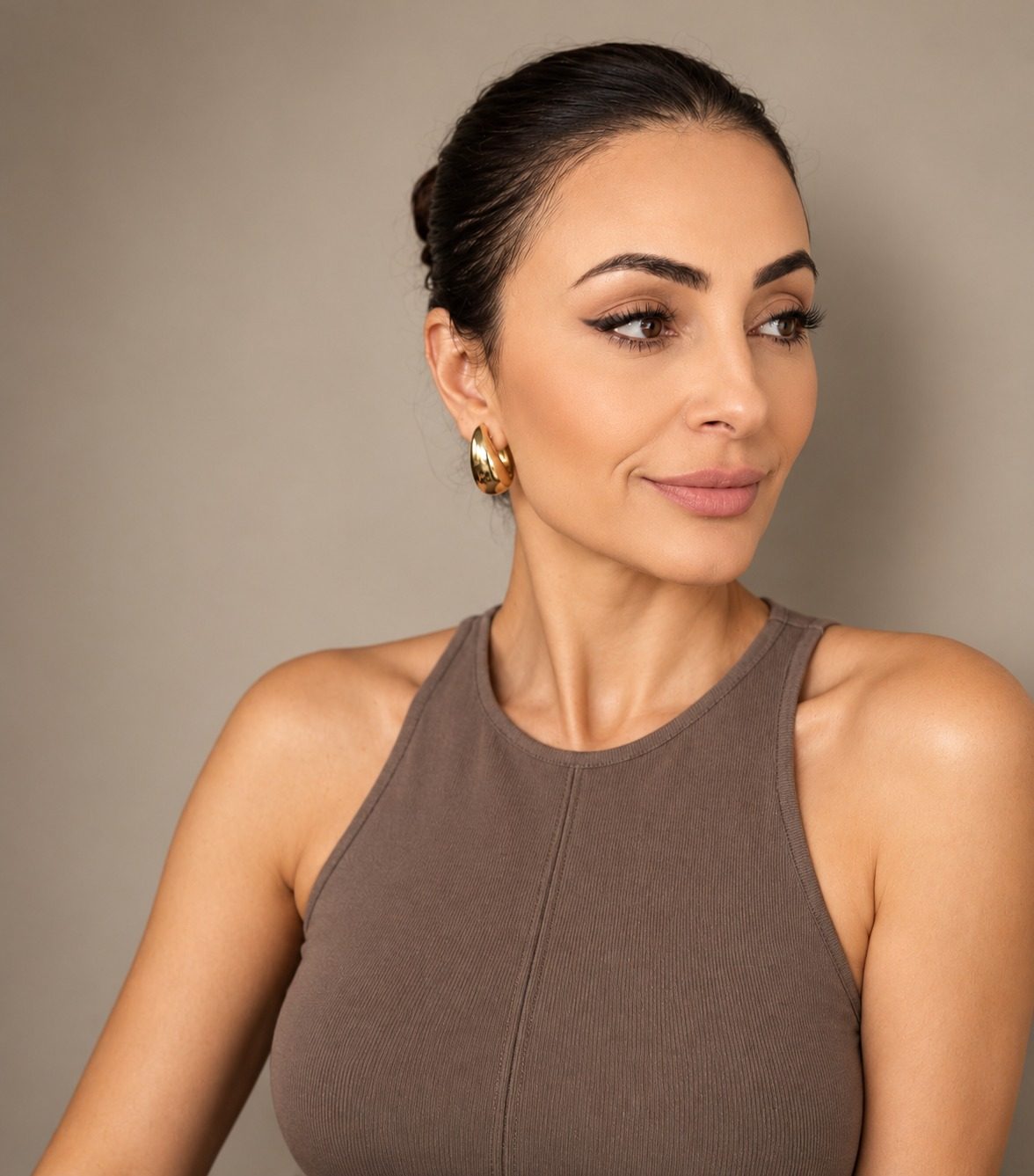 Studio portrait of Anna Agajanyan in a taupe top with gold earrings, looking to the side