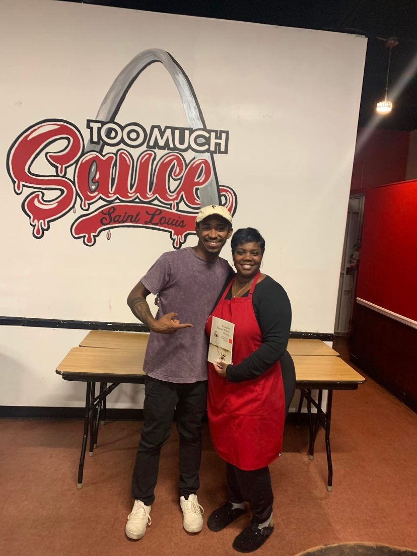 Ardimus Caldwell Jr. with a Too Much Sauce St. Louis team member in front of the restaurant's Gateway Arch mural