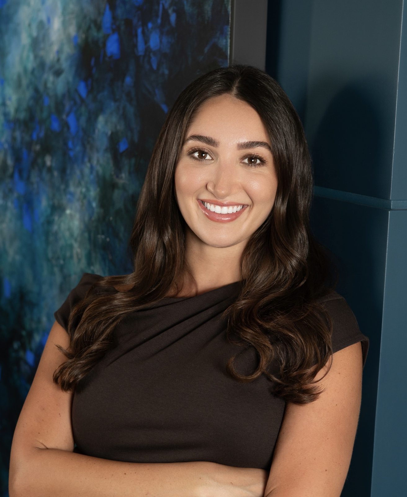 Ariana Stanley, founder and creative director of Creative Concepts Agency, smiling in a brown dress in front of a blue abstract painting