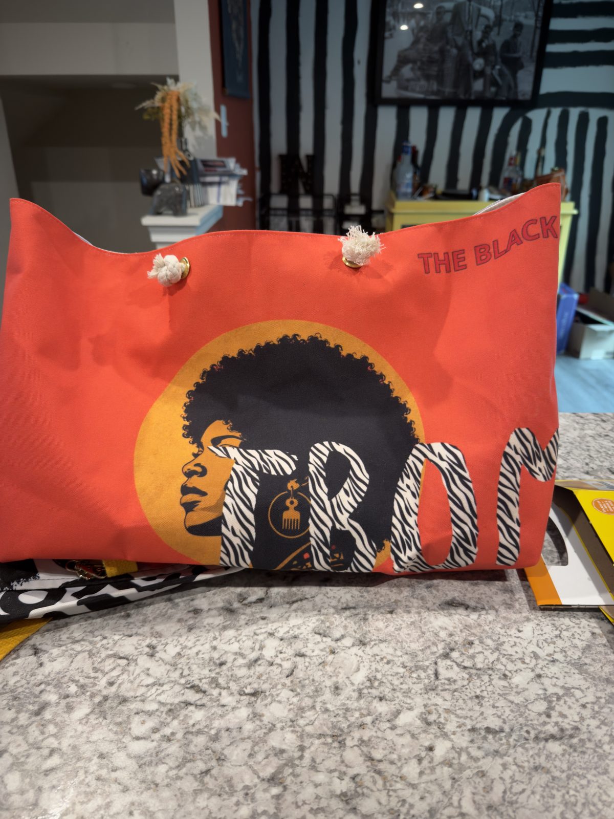 TBOM Apparel tote bag with the brand’s design of a woman with an afro in profile against an orange sun