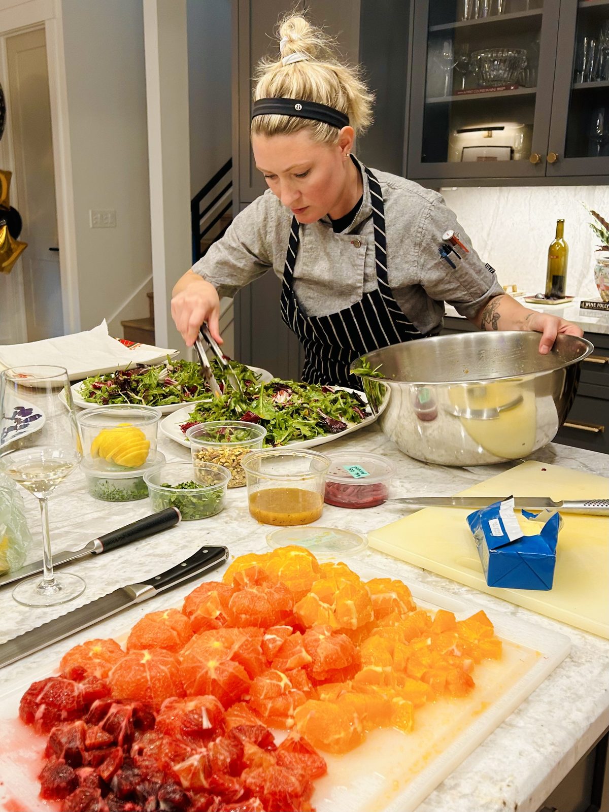 Ashley Ondrick tossing a salad in a client's kitchen beside a board of diced citrus