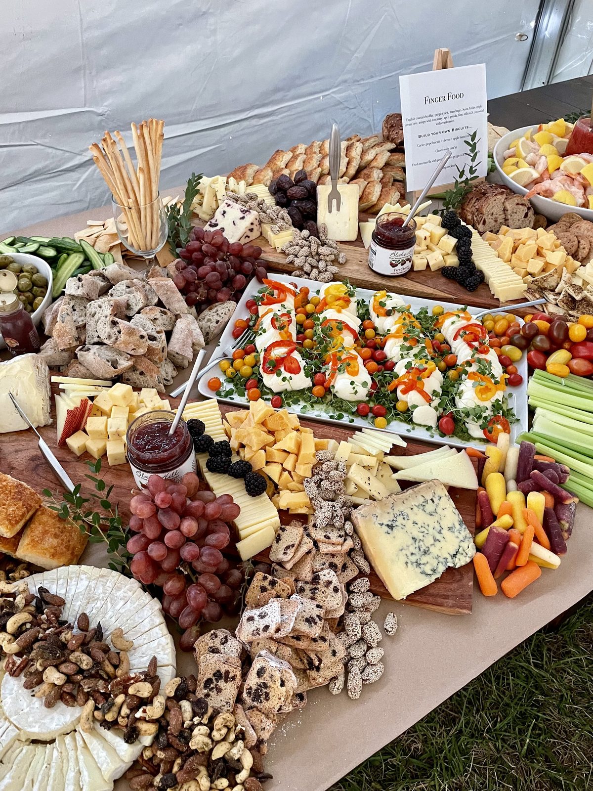 Grazing table under a tent with cheese boards, caprese skewers, breadsticks and fruit