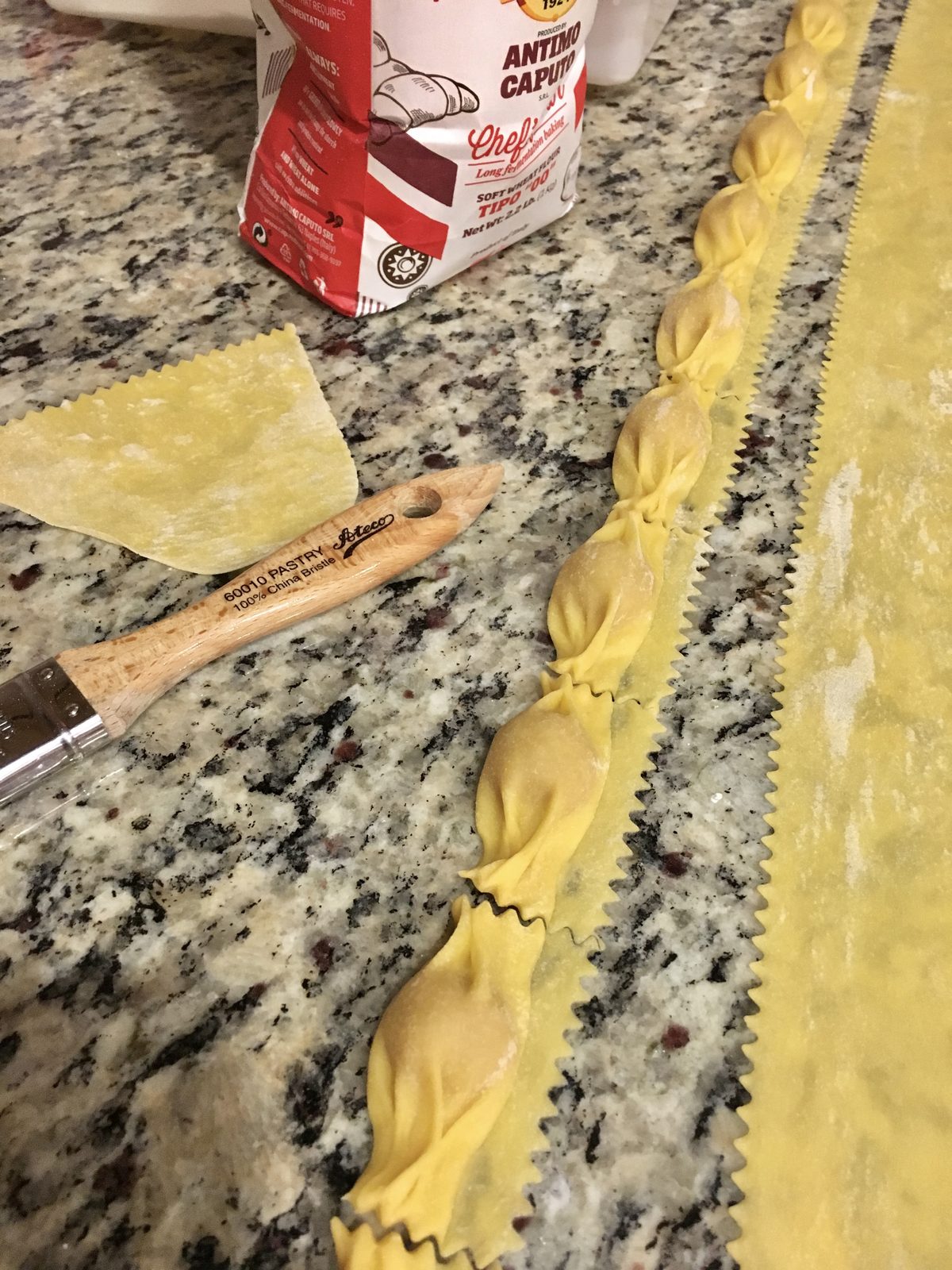 Fresh handmade pasta with crimped edges on a granite counter next to a pasta cutter