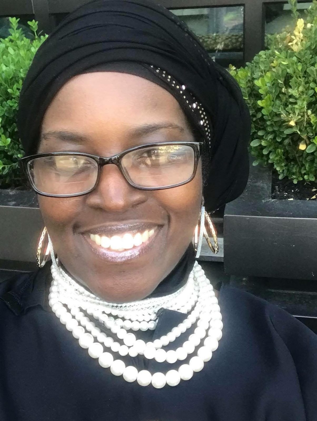 Athenae Evans, Administrator of Roxborough Home for Women, smiling in glasses, a black head wrap and layered pearl necklaces