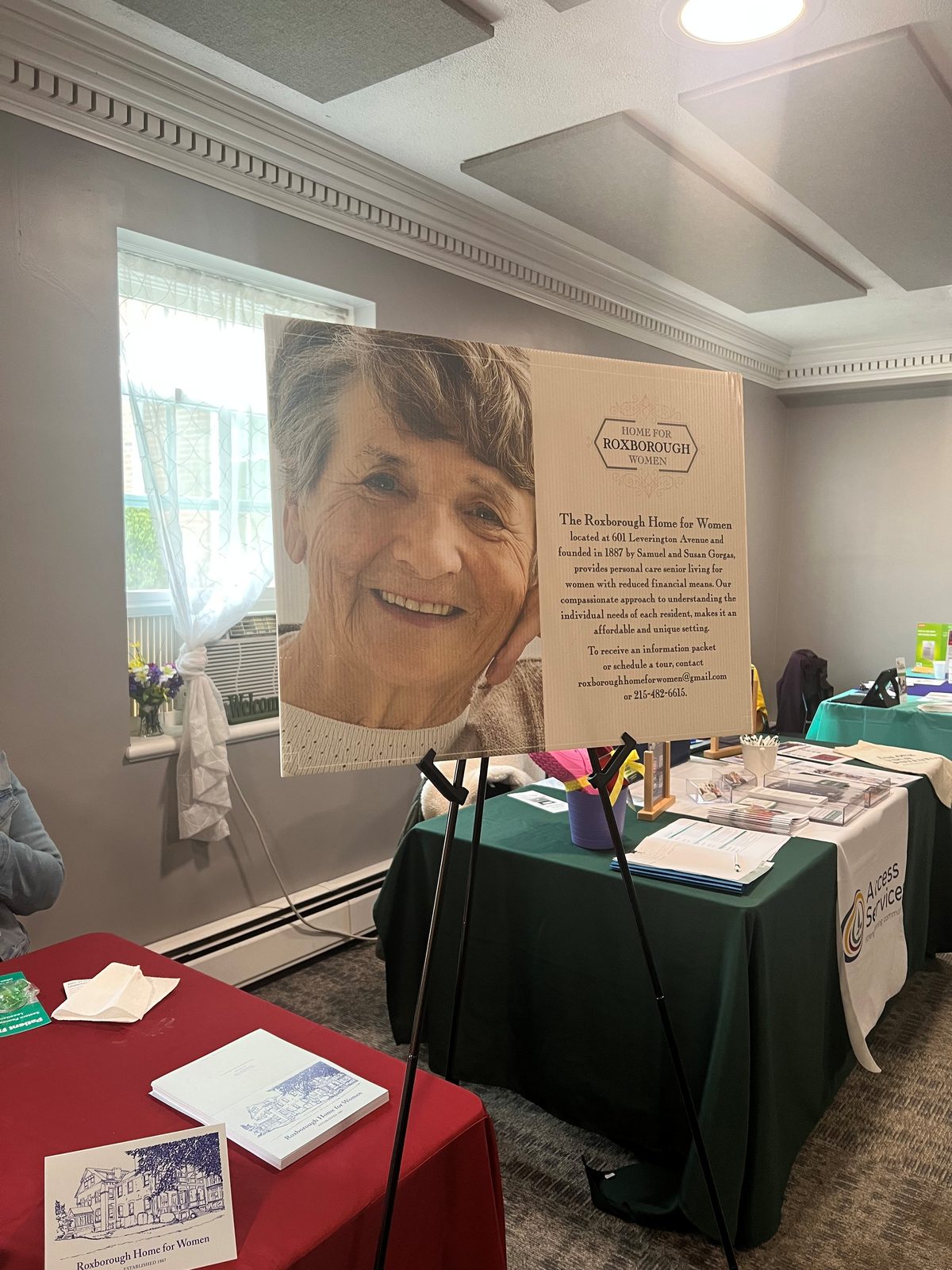 A Roxborough Home for Women display board with a smiling resident on an easel at a health and wellness expo