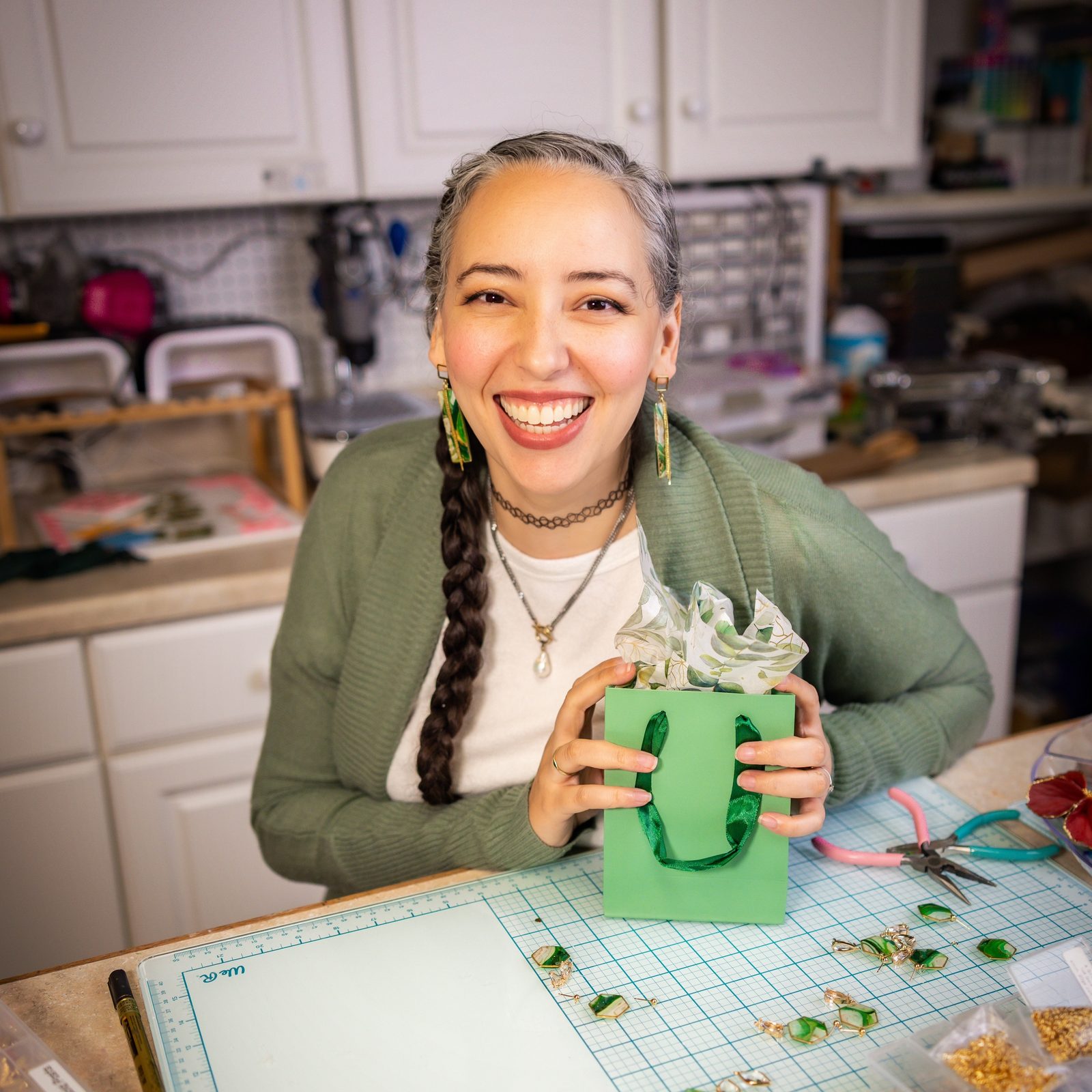 Brittany Arnett, founder of The Dappled Wood, laughing at her studio workbench in a green cardigan with a long braid