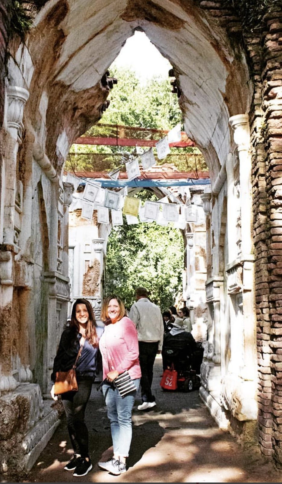 Carmen Holley, right, with a travel companion under a stone archway hung with prayer flags