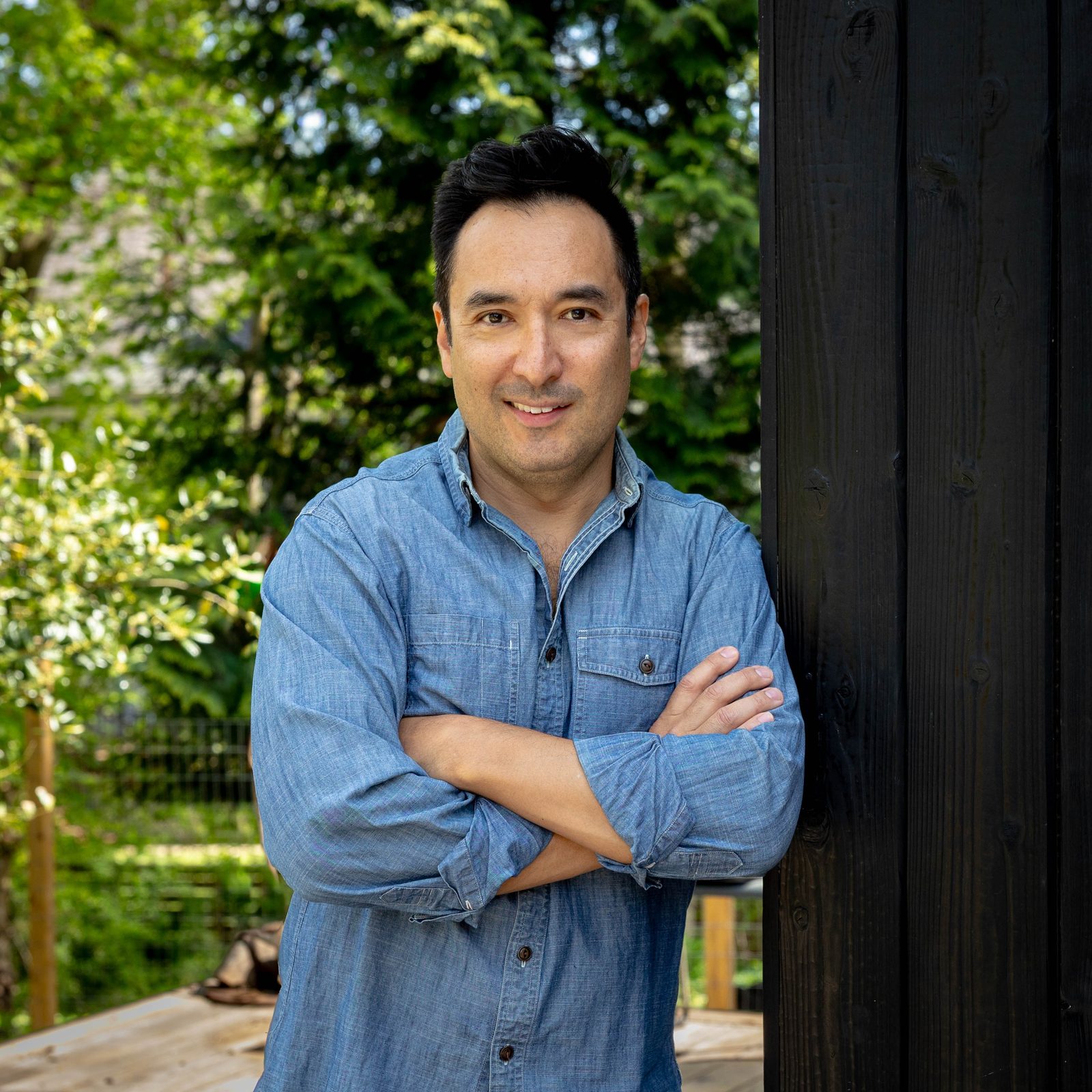 Chris Kao, founder of Tsung Haus Design, in a denim shirt with arms crossed beside a black-stained timber wall