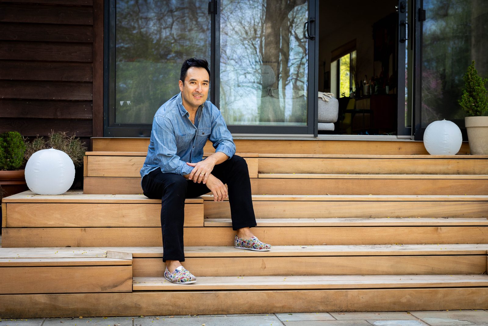 Chris Kao seated on wide wooden deck steps outside a house with sliding glass doors