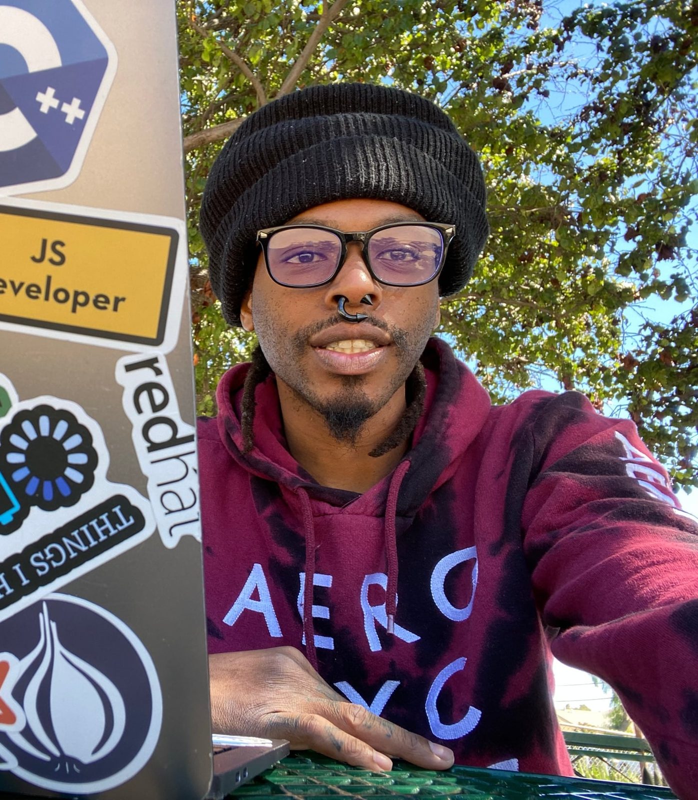 Clinton Robinson Jr., founder of Chefry, in a black beanie and glasses at a park table beside his sticker-covered laptop
