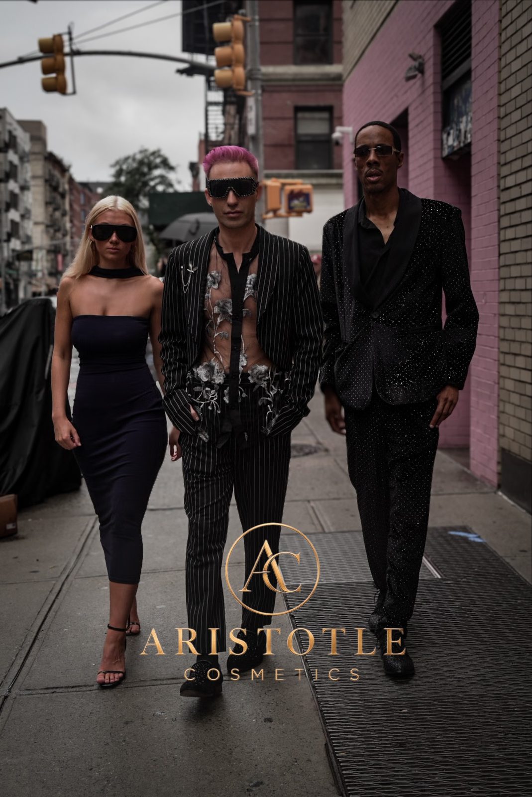 Three people in black evening wear and sunglasses walking down a New York City street, with the Aristotle Cosmetics logo in gold