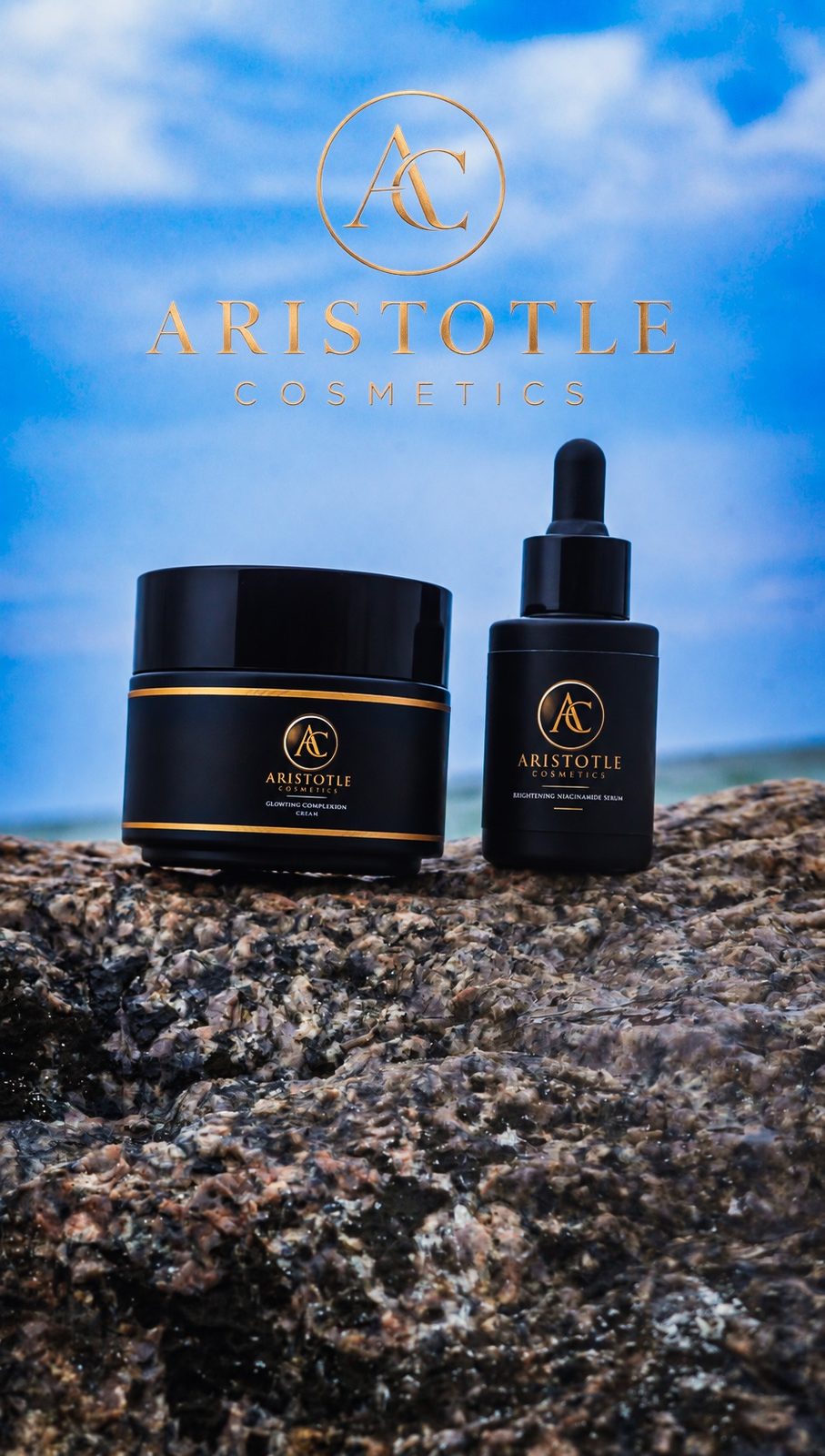 Aristotle Cosmetics cream jar and serum bottle in black and gold on a granite rock by the sea