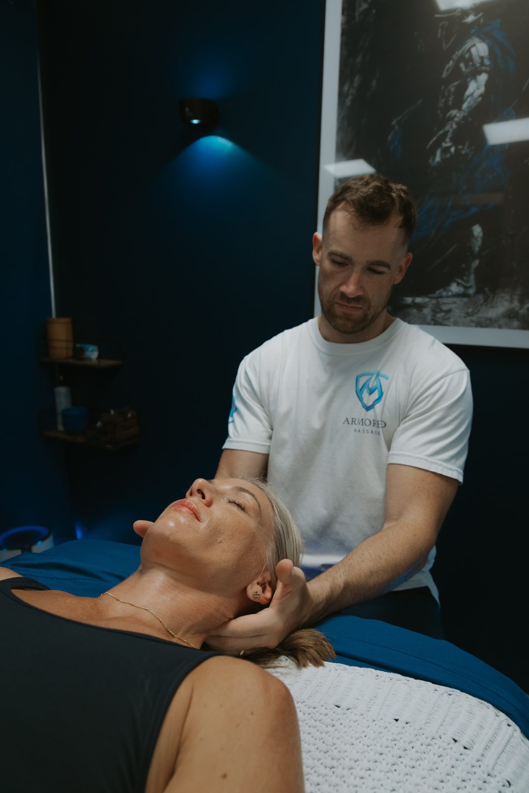 Stephen Preyer, a licensed massage therapist, working on a client's neck and shoulders in a dark blue treatment room