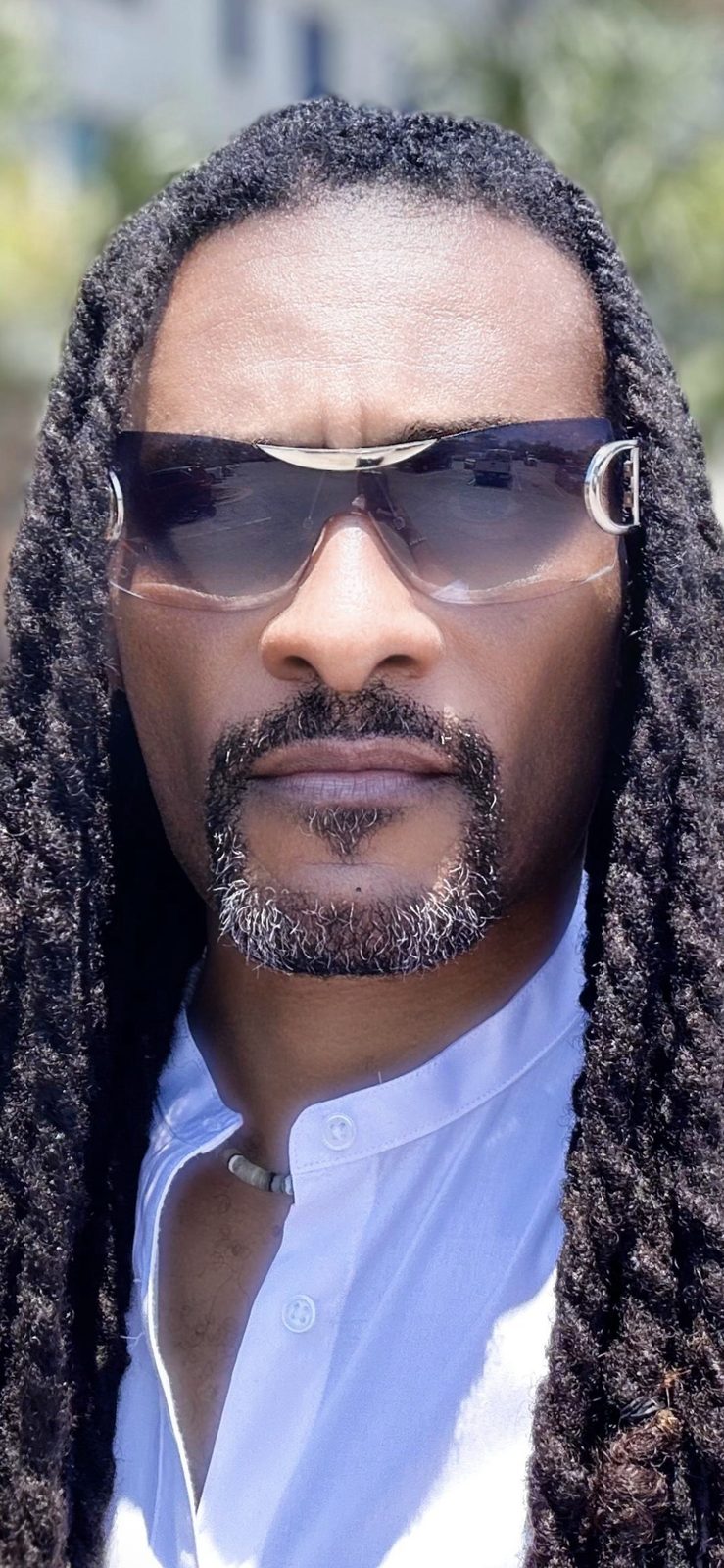 Dearick Milton, founder of Sugar Bee's Boy, LLC, in sunglasses and a white shirt with long locs over his shoulders