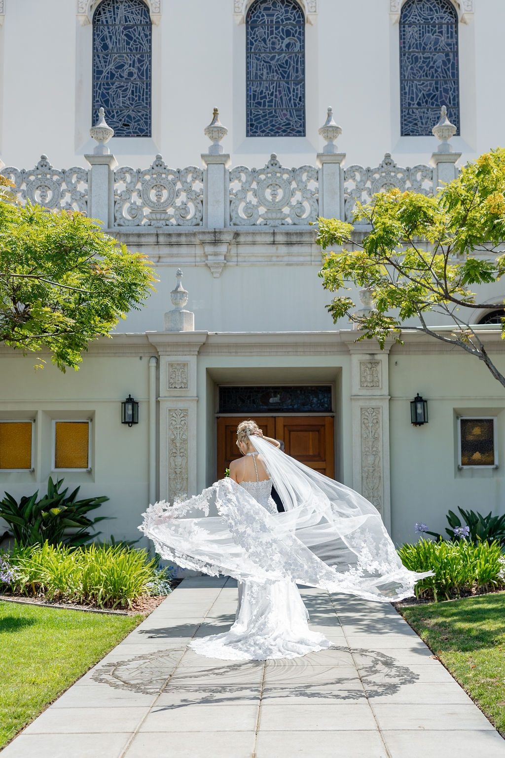 A bride with her veil in the wind outside a white chapel, photographed by Divya Stumpff