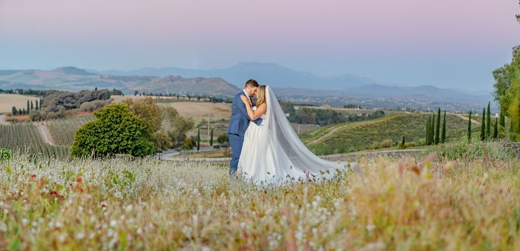 A couple embracing in a hillside field above the vineyards at dusk, photographed by Divya Stumpff