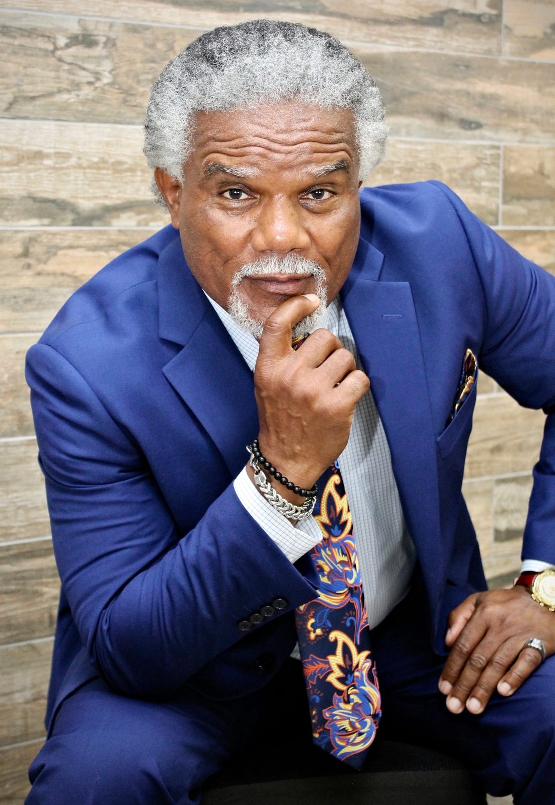 Donald L. Dowridge, Jr., founder of DLD Enterprises, in a royal blue suit and paisley tie, resting his chin on his hand