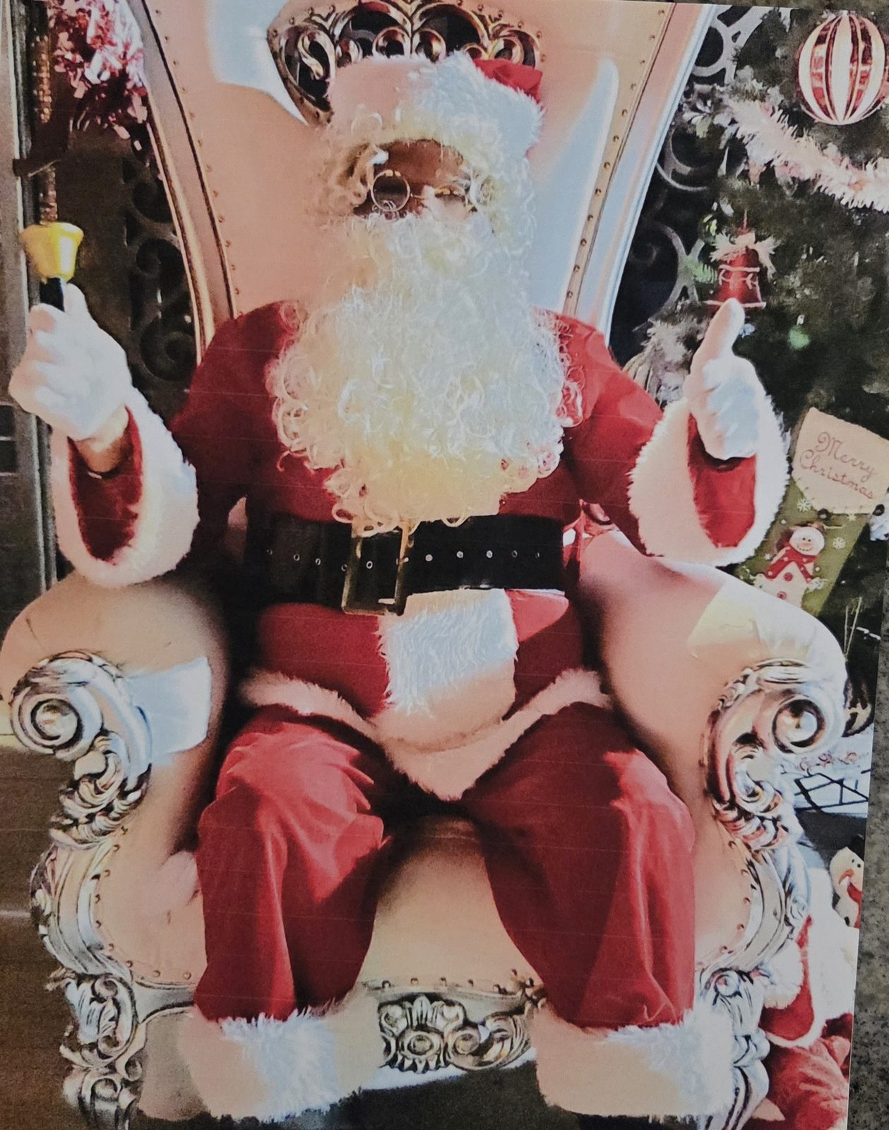 Donald L. Dowridge, Jr. as Santa, seated on an ornate throne beside a Christmas tree and giving a thumbs up