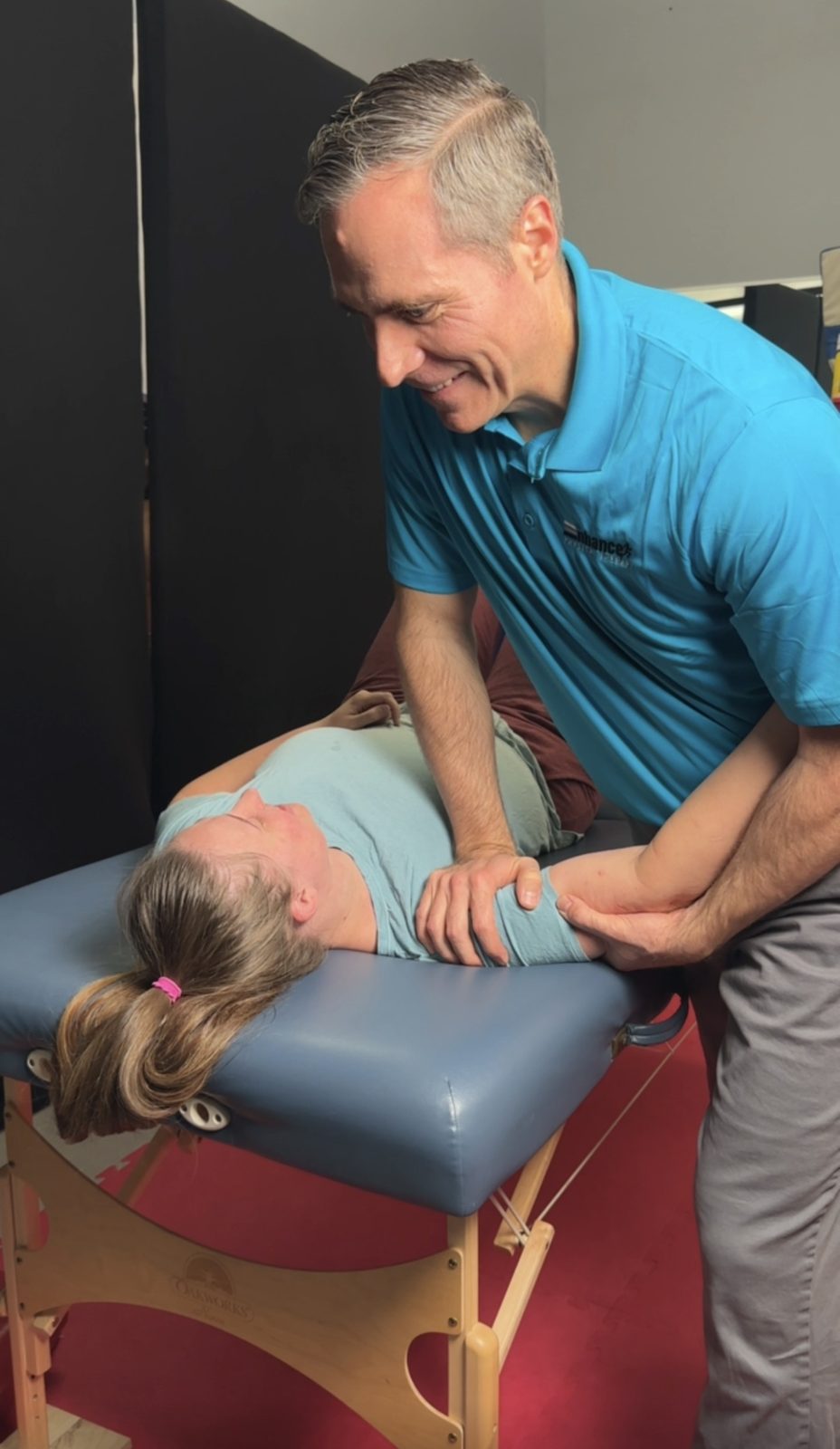 Dr. Doug Ashton working on a patient's shoulder as she lies on her side on a treatment table