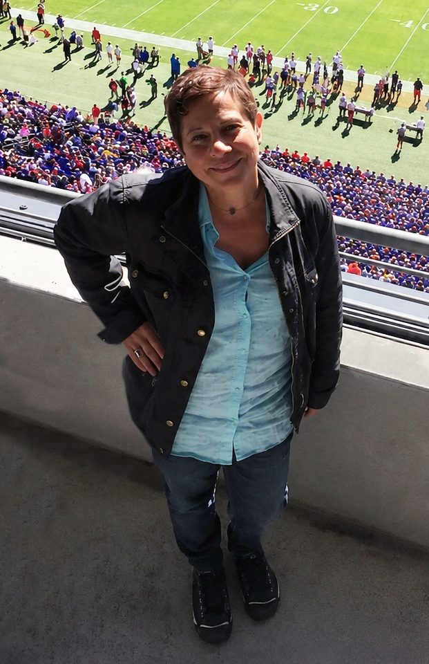 Emily Goldstein standing at a stadium railing with a crowd dressed in purple filling the stands behind her