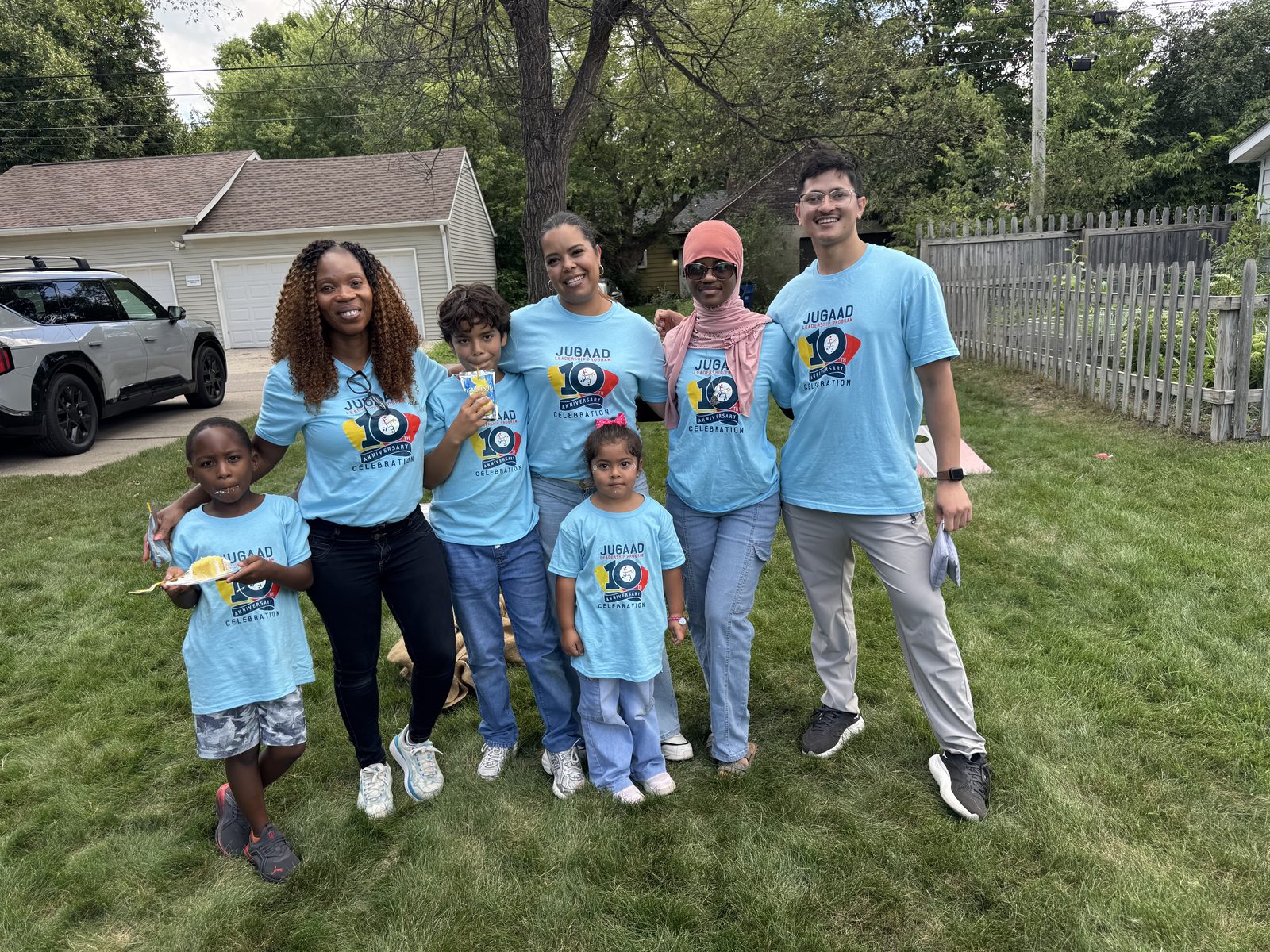 Jugaad community members and children in matching tenth-anniversary T-shirts gathered on a lawn