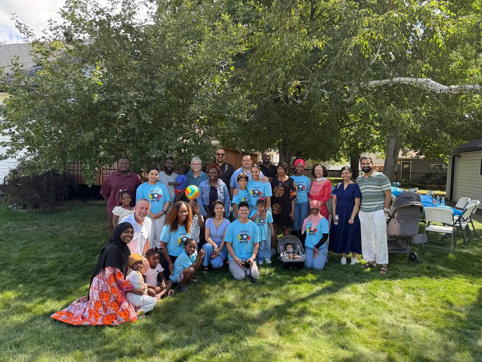 A large group of Jugaad community members and families gathered under trees at an outdoor celebration