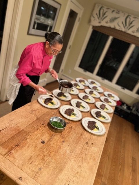 Chef Felicia plating a course for a dinner party on a long wooden table