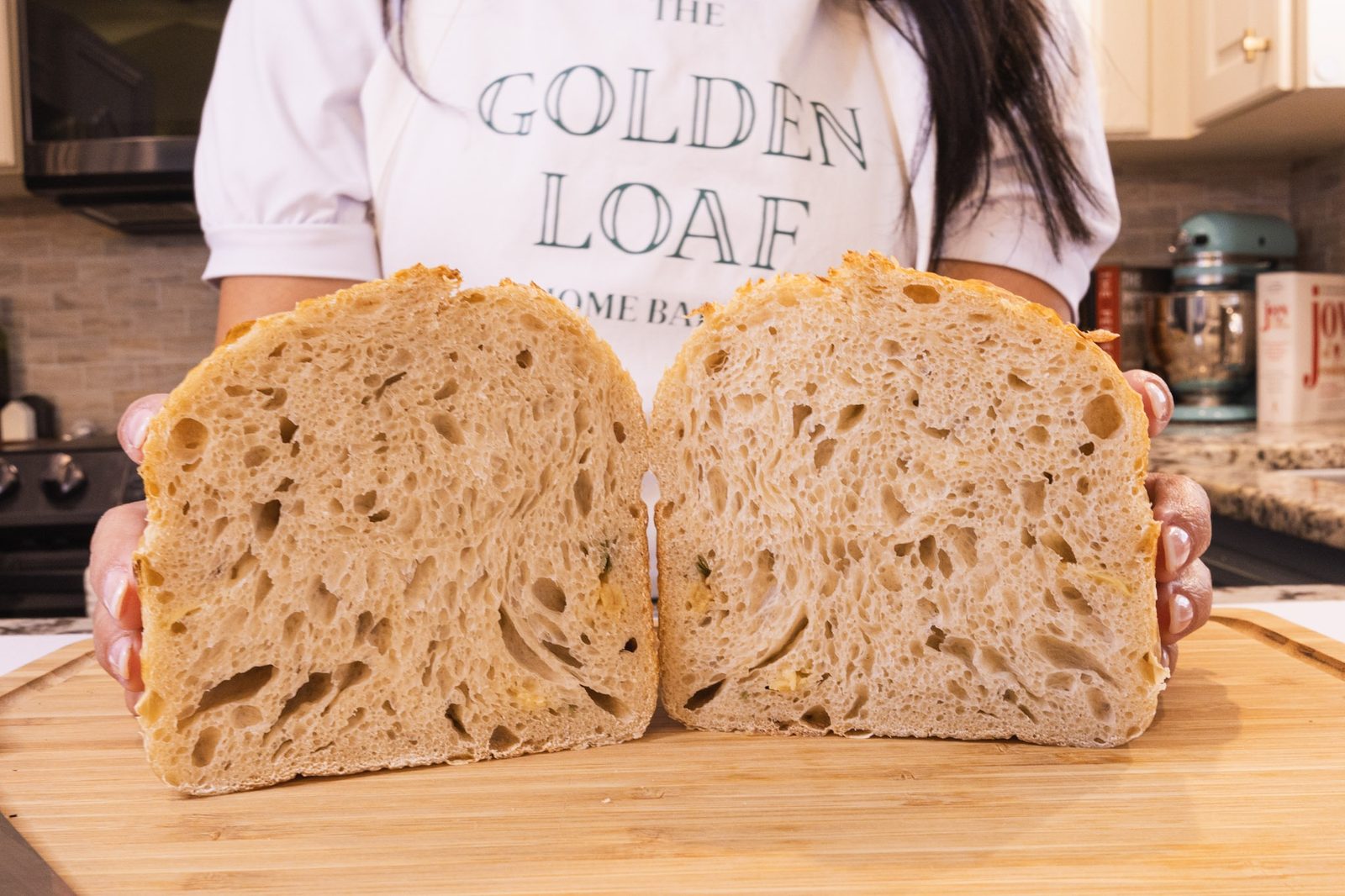 Two halves of a freshly cut sourdough loaf held up on a cutting board, showing the open crumb