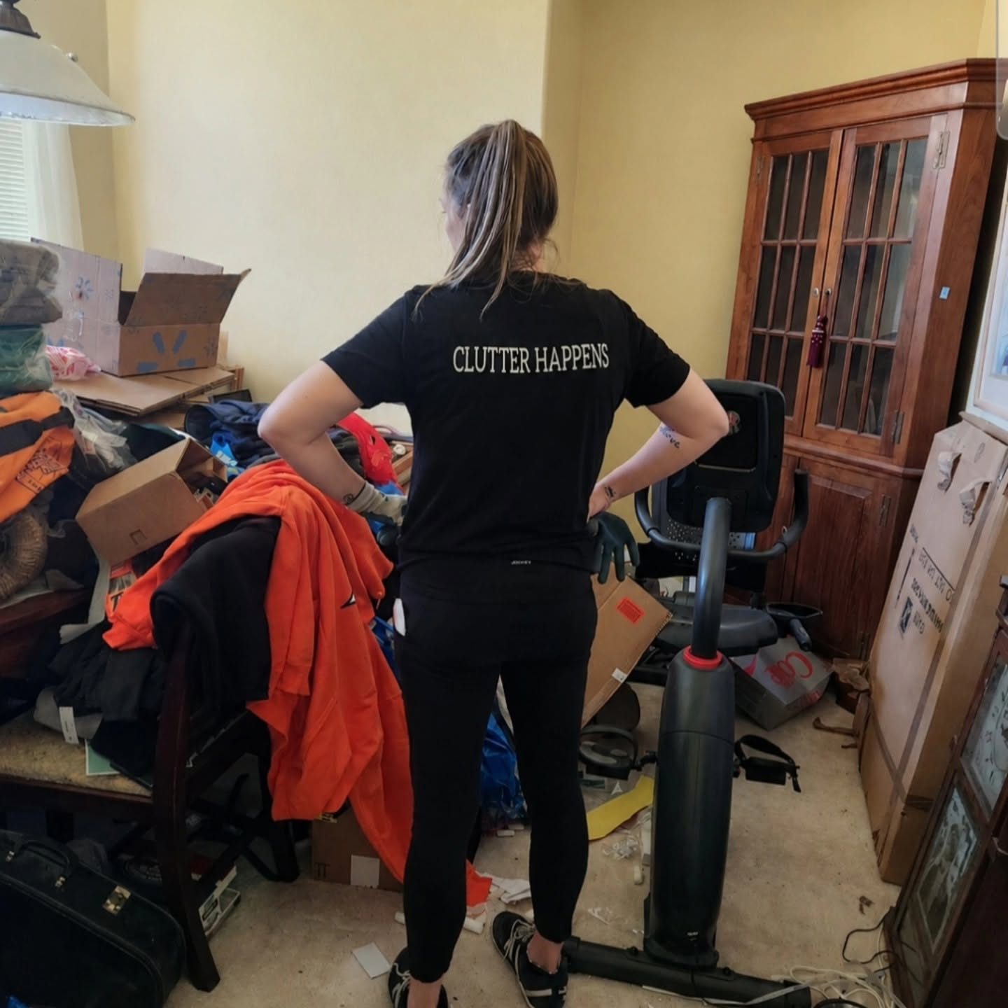 Grace Hall in a Clutter Happens T-shirt, surveying a cluttered client room before organizing it