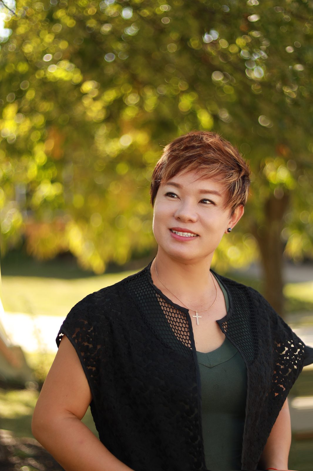 Grace Liu, owner of Infinity Massage in Kansas City, smiling outdoors in a black lace cardigan and green top
