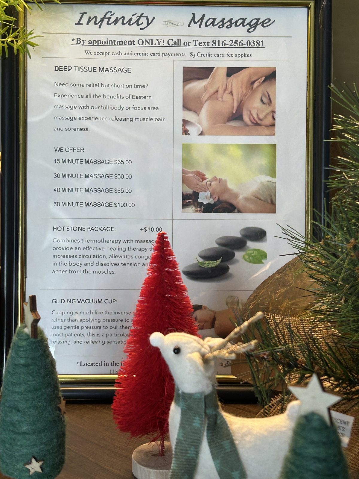 The framed Infinity Massage service menu listing deep tissue, hot stone and cupping options, beside a small Christmas tree and a felt reindeer