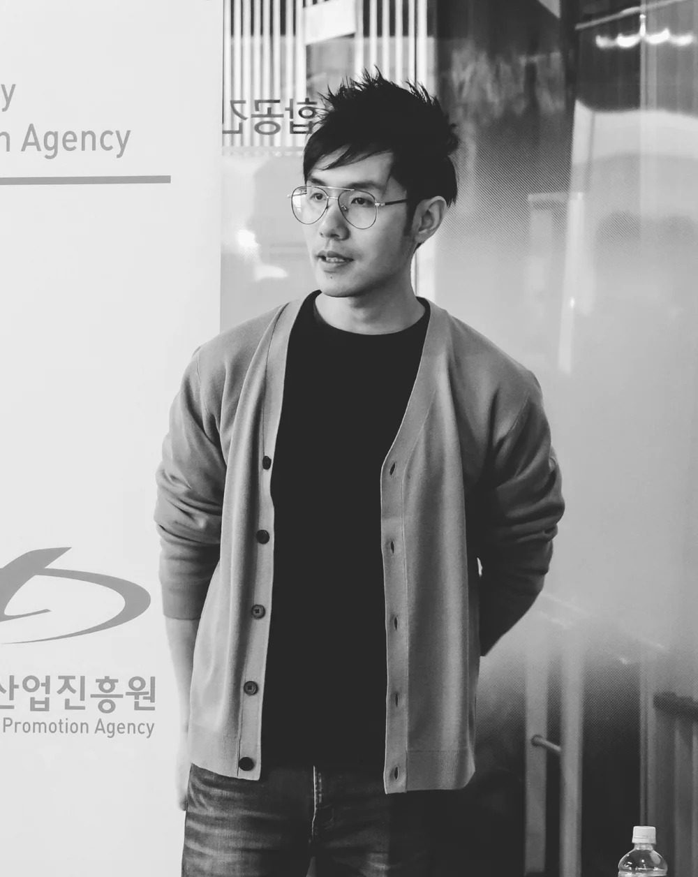 Gregory Tan, composer and founder of Soul Forest Music, in glasses and a grey cardigan at the Busan sync music conference, black and white