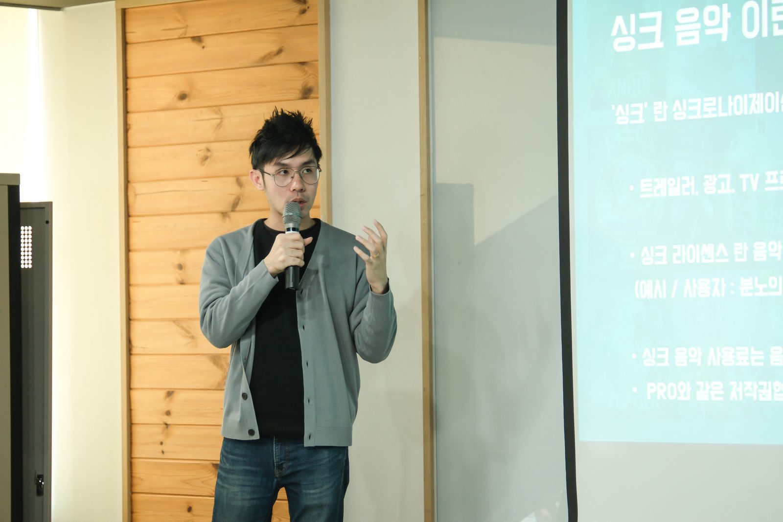 Gregory Tan speaking into a microphone in front of a projected Korean-language slide about sync music