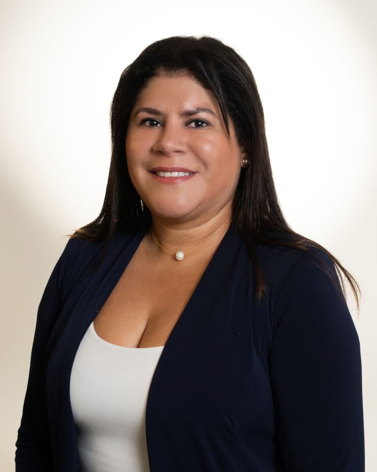 Hilda Rodriguez, founder of Dahil Bar in Miami, in a navy blazer and pearl necklace against a cream backdrop