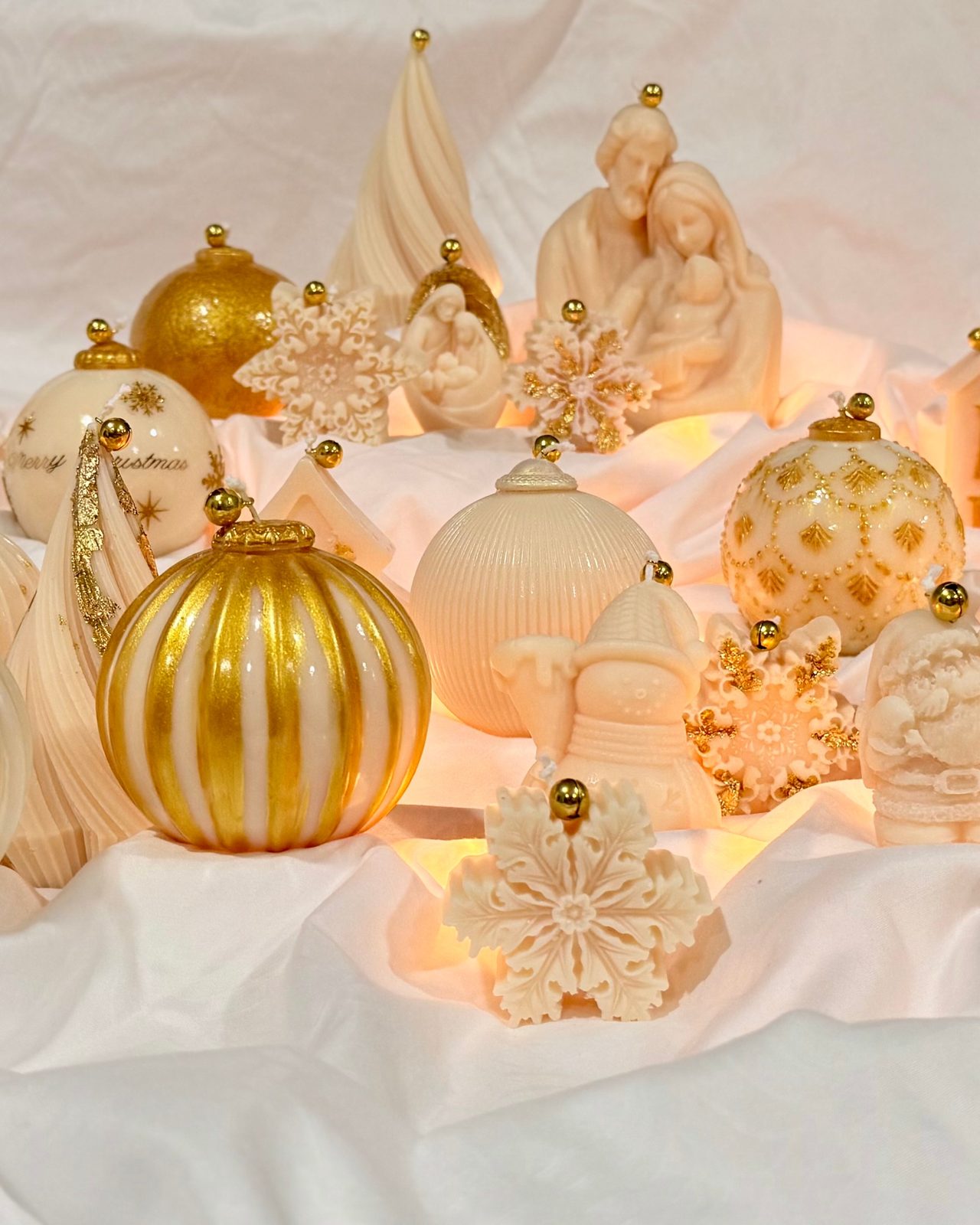 Dahil Bar holiday candle collection in cream and gold: ornament spheres, snowflakes, a nativity scene and a snowman on white fabric
