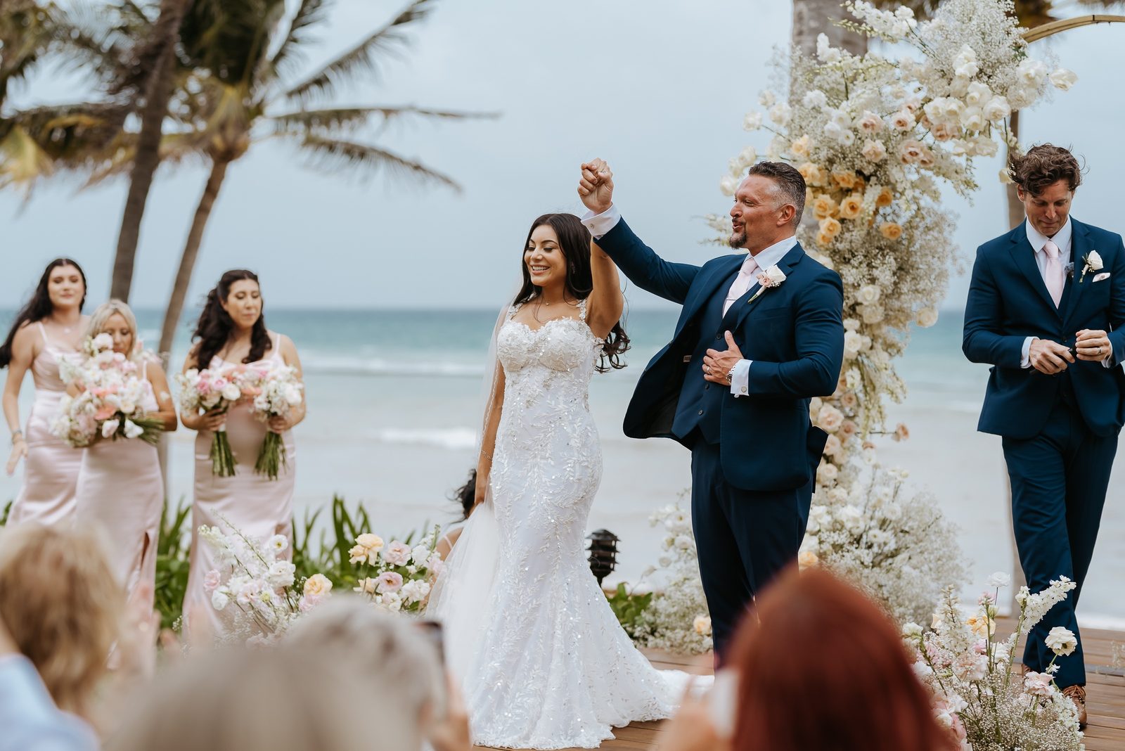 A bride and groom celebrating at a beach wedding ceremony with their wedding party, photographed by Idaly Bustamante