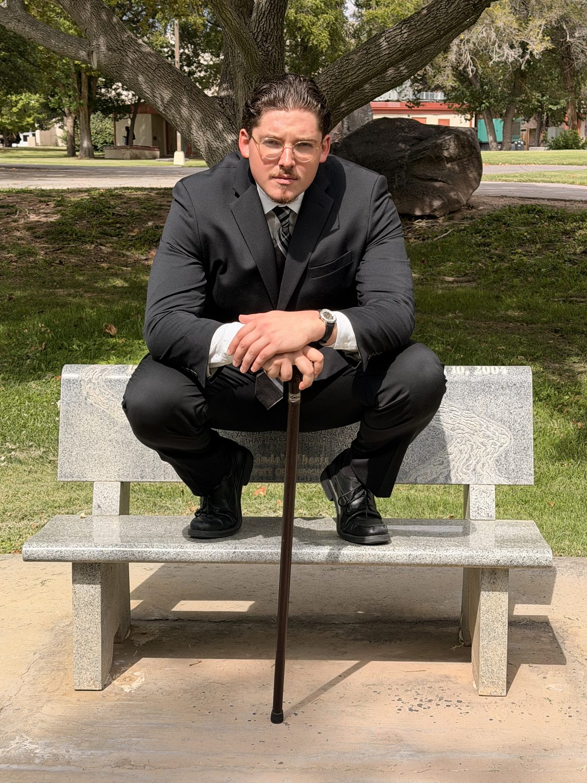 Jacob Sneed, founder of Incendiary Concepts, seated on a stone bench in a dark suit with a walking cane