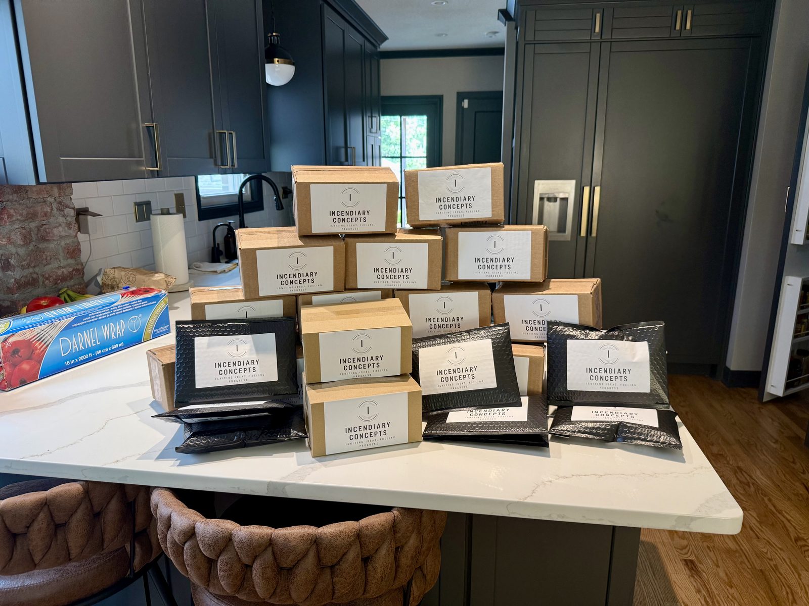 Stacks of packed Incendiary Concepts orders in branded boxes and black mailers on a kitchen counter