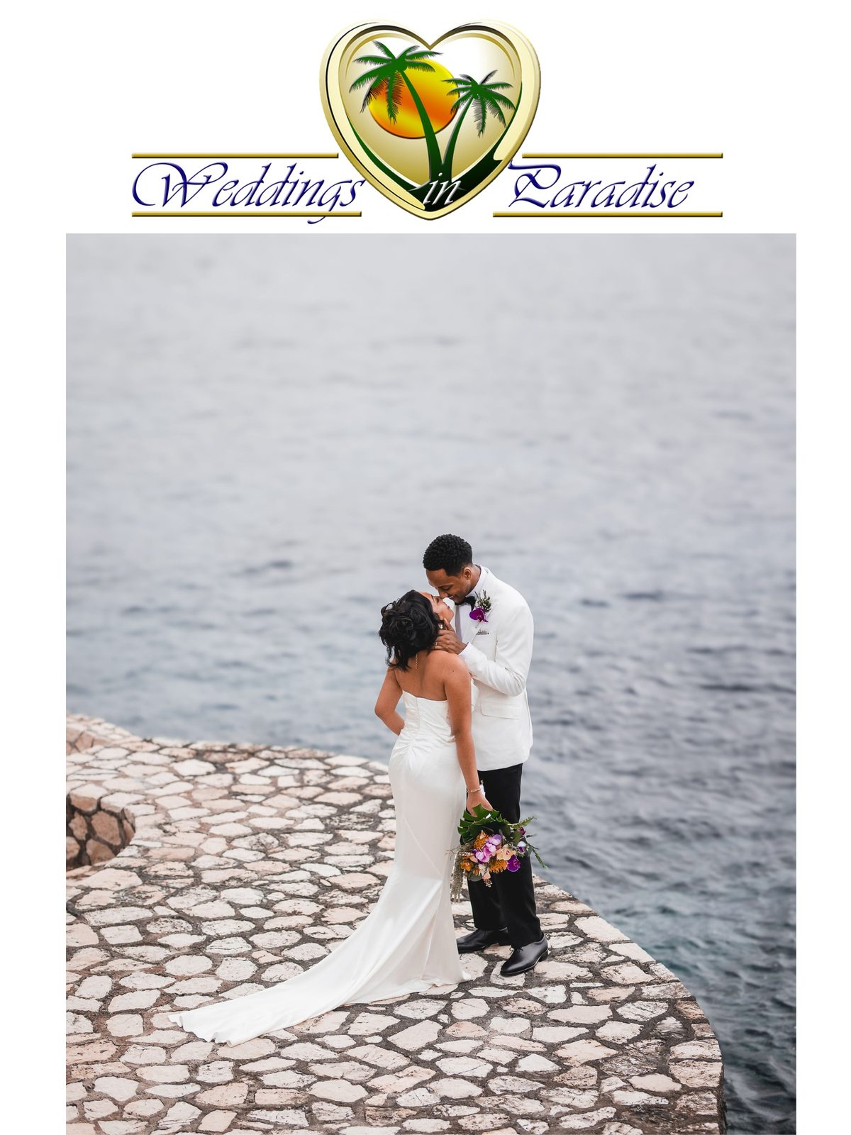 A bride and groom kissing on a stone cliff edge above the sea beneath the Weddings in Paradise logo