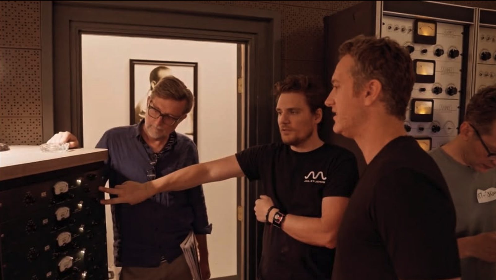 Joshua M. Lutz in a JML Studios T-shirt pointing out outboard gear to two colleagues in a studio control room