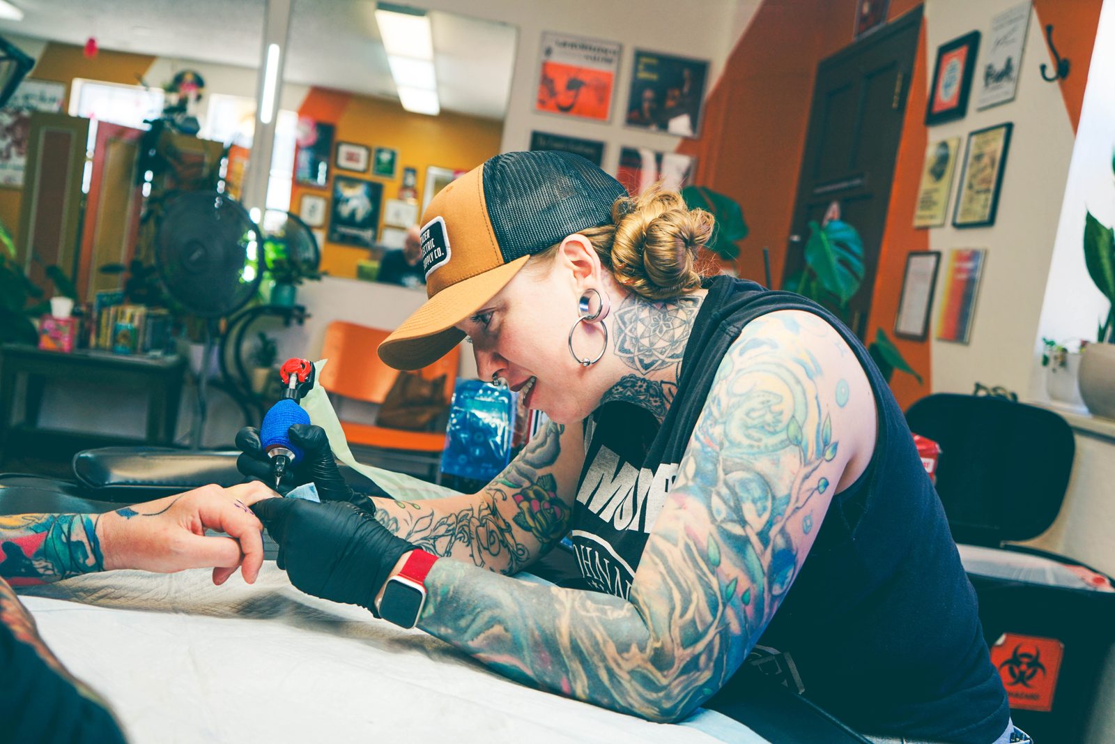 Kate Grinstead, arms covered in tattoos, tattooing a client in the colourful Zeitgeist studio