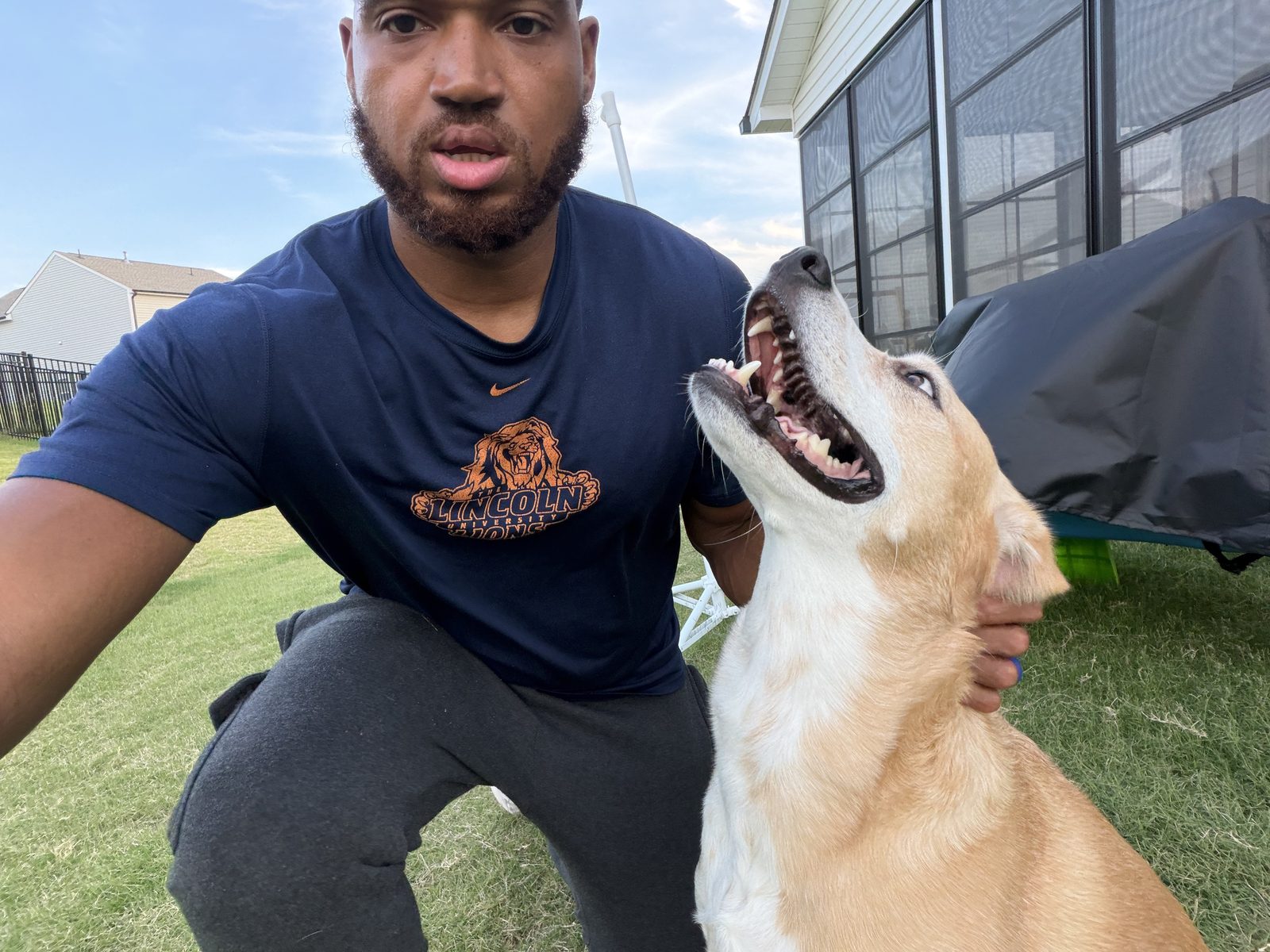 Lance Felder kneeling on a lawn with his arm around a happy tan dog