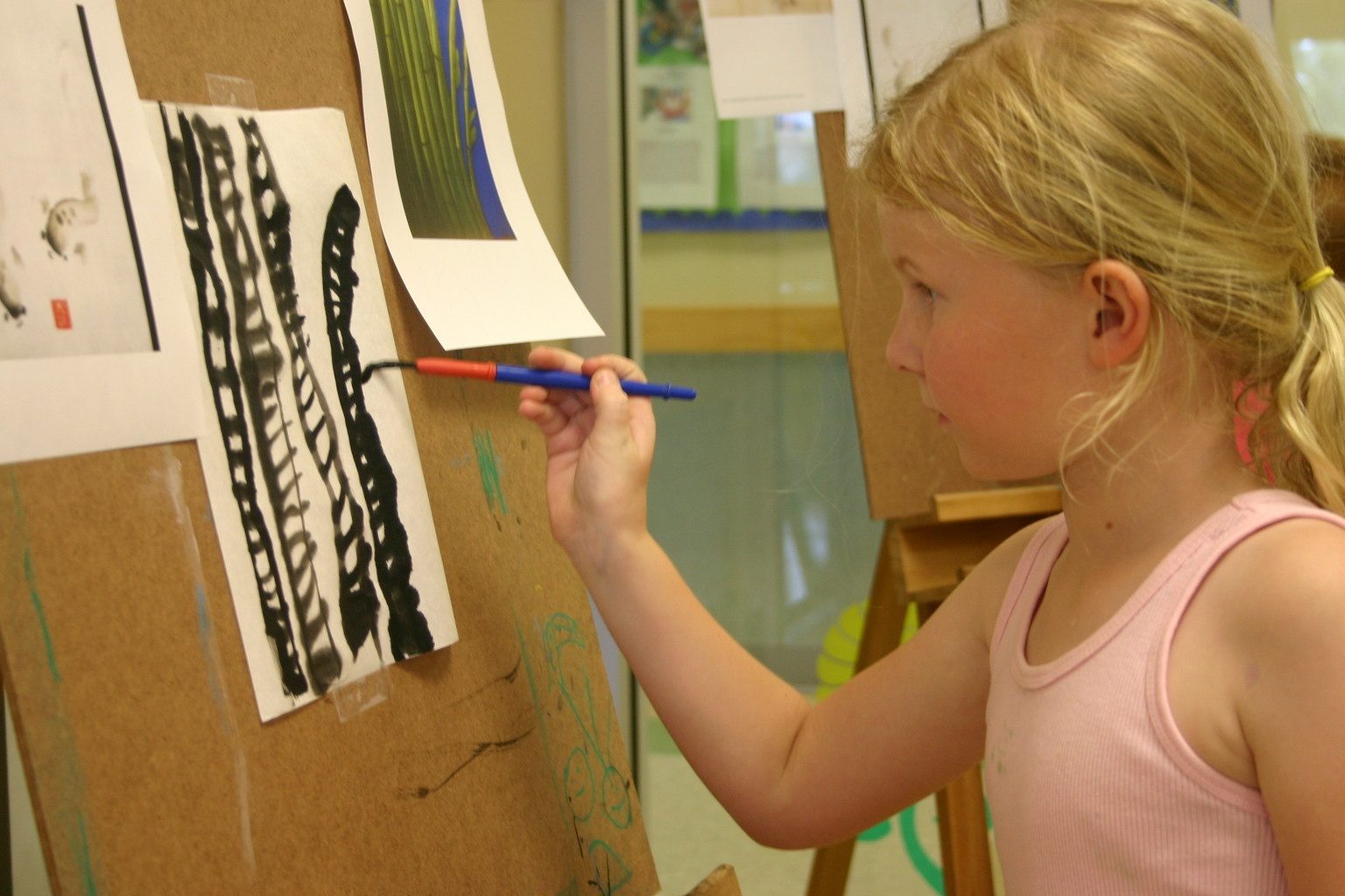 A Lupine Lane student painting black brushstrokes on paper pinned to an easel