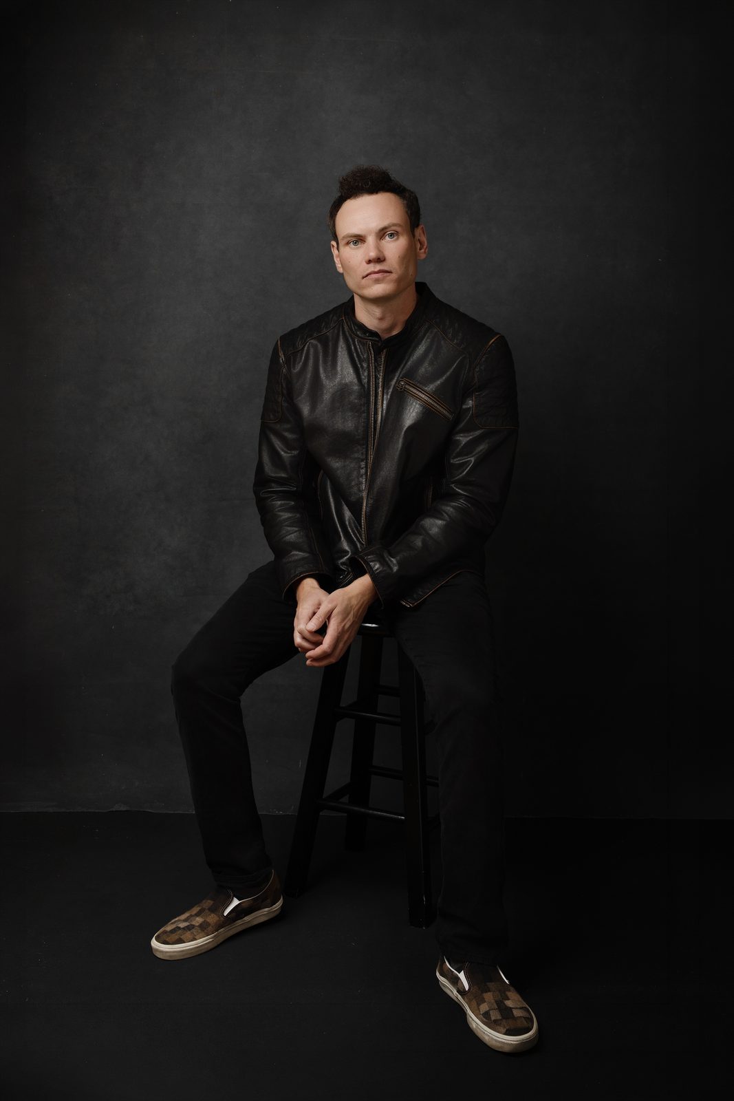 Michael Cecchinelli, founder of Solveig Pictures, seated on a stool in a black leather jacket against a dark studio backdrop