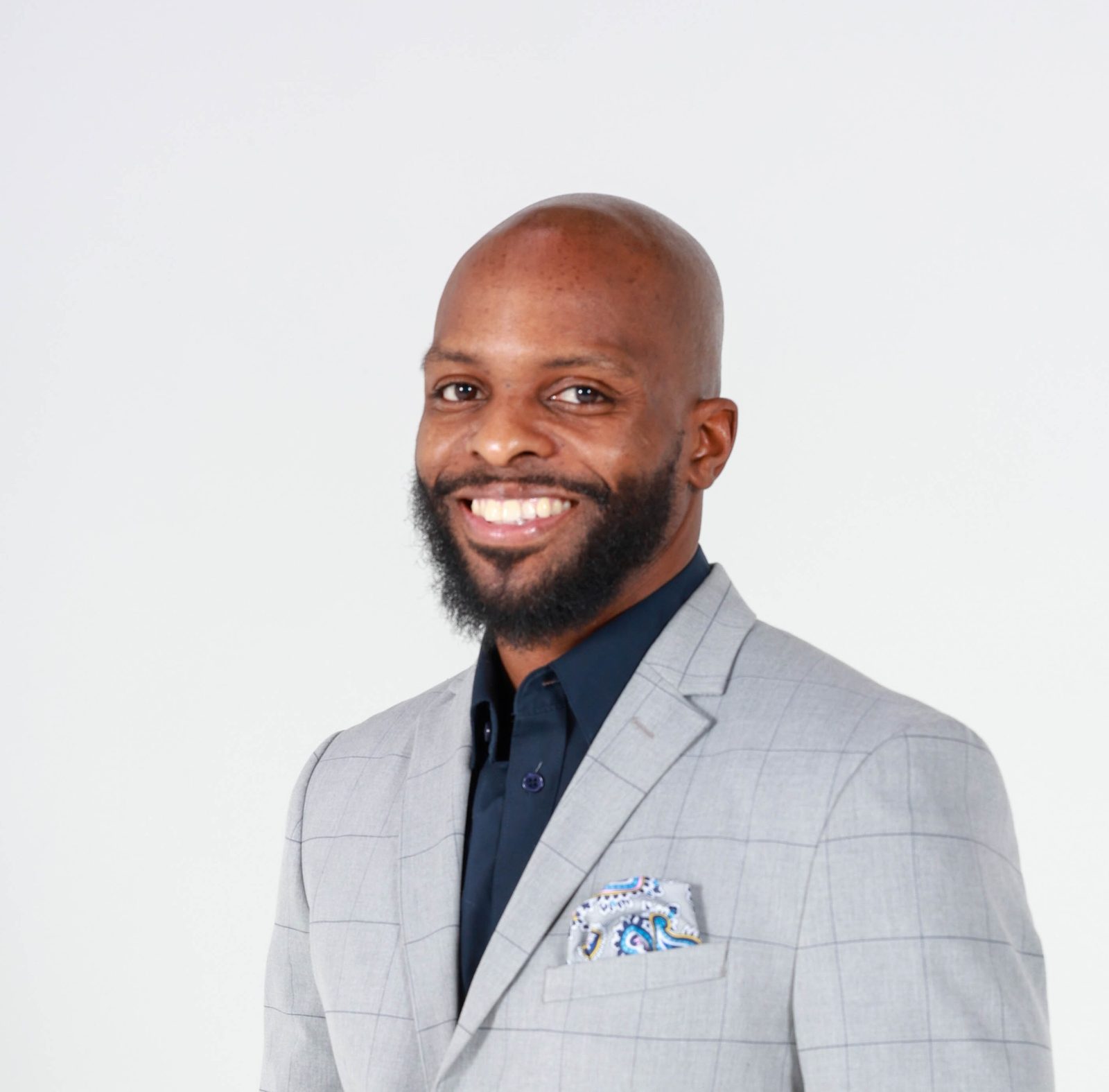 Milton Putman in a grey windowpane blazer, navy shirt and patterned pocket square