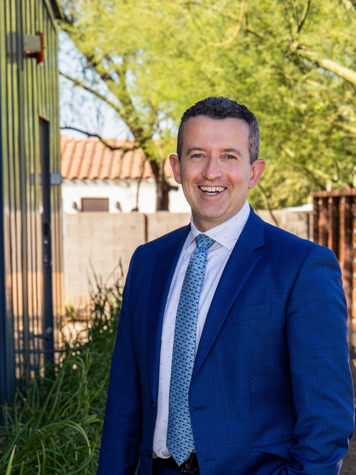 Oleg Bortman, co-founder of The Brokery, smiling in a blue suit and patterned tie outside in Phoenix, Arizona
