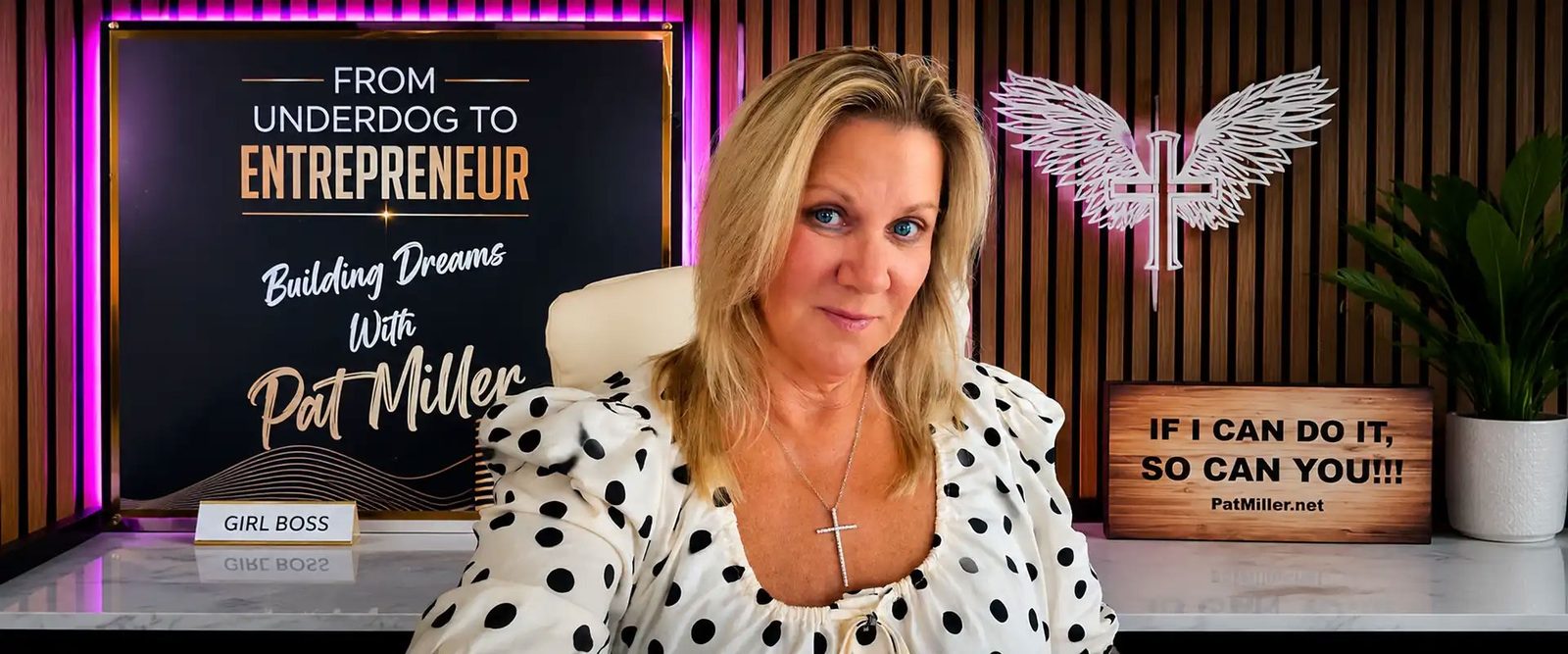 Pat Miller in her podcast studio, in front of the From Underdog to Entrepreneur: Building Dreams with Pat Miller sign